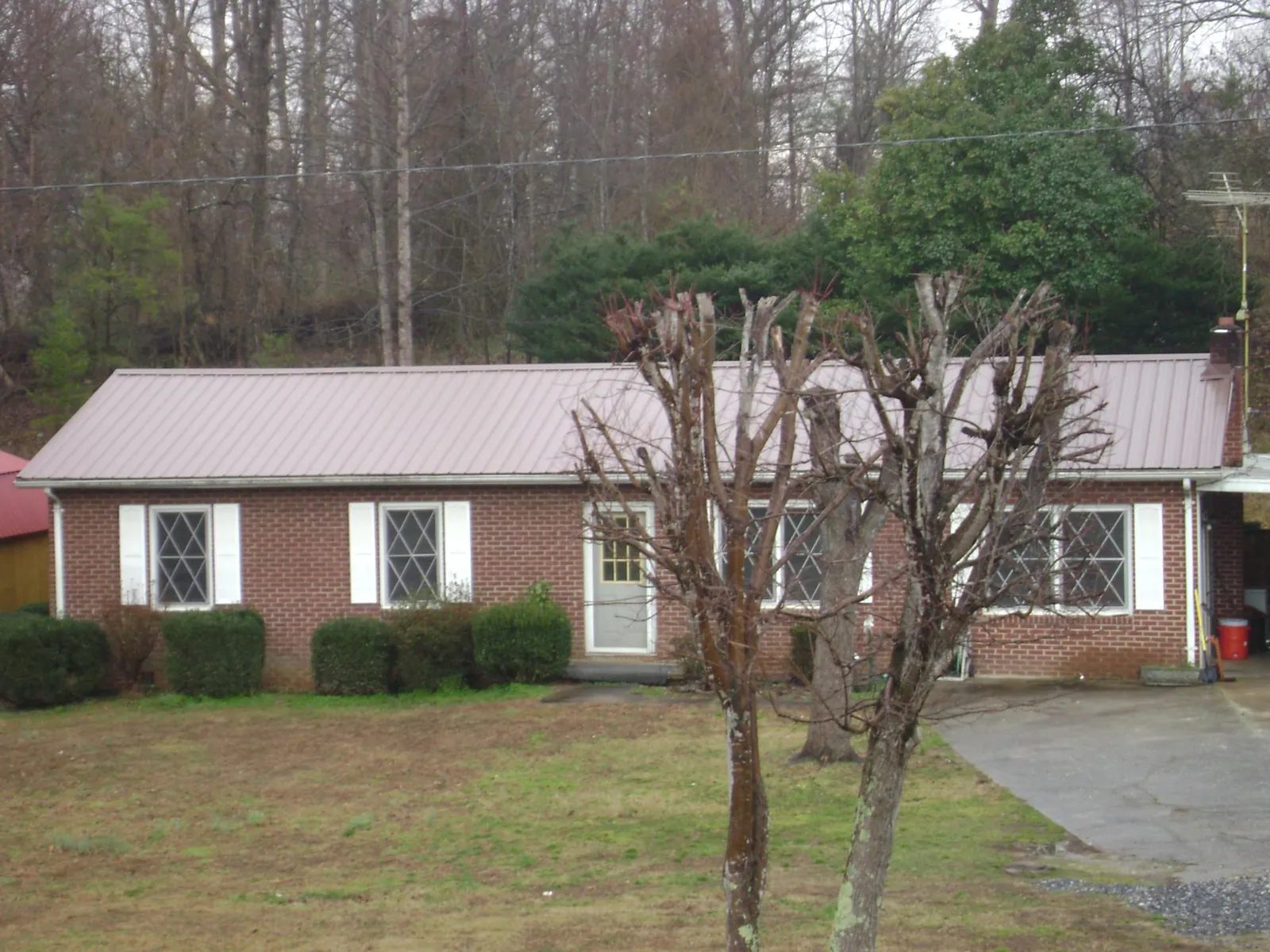 Mauve metal roof on a brick ranch home behind bare trees in Magnolia