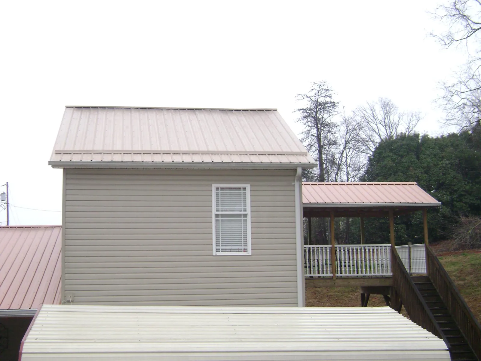 Tan metal roofs on a two story addition and attached porch, from a Roof Replacement job in Magnolia